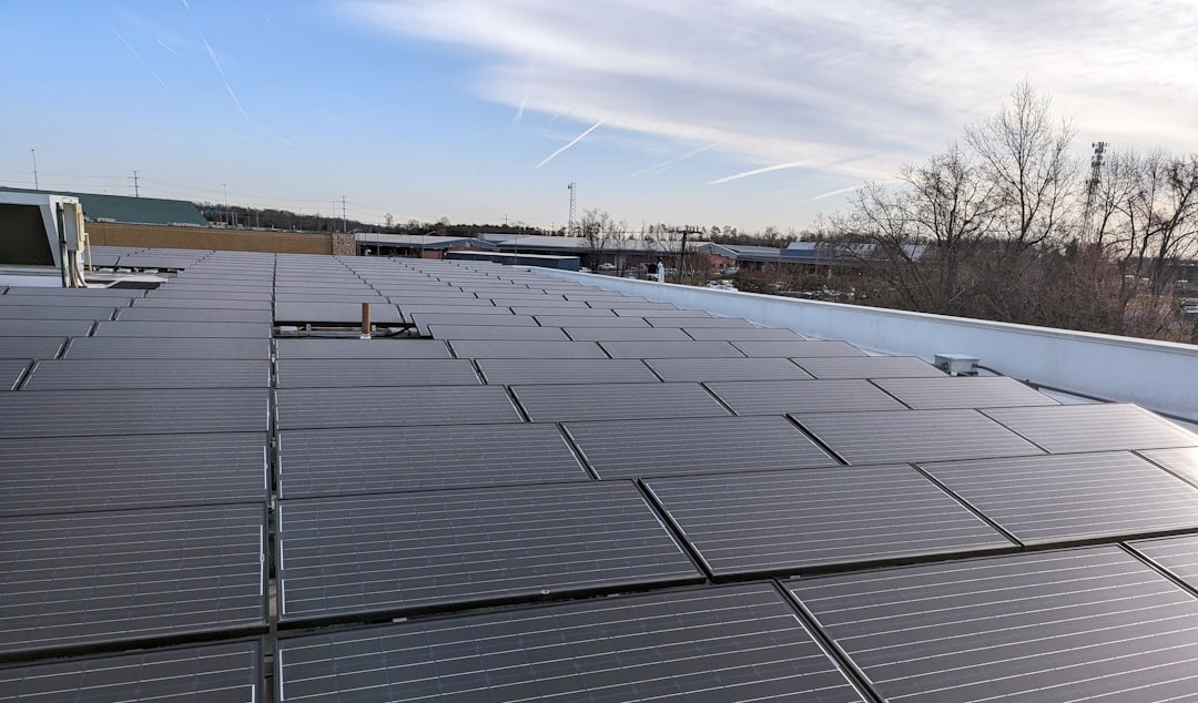 Dark solar panels arranged on a commercial rooftop under a bright sky.